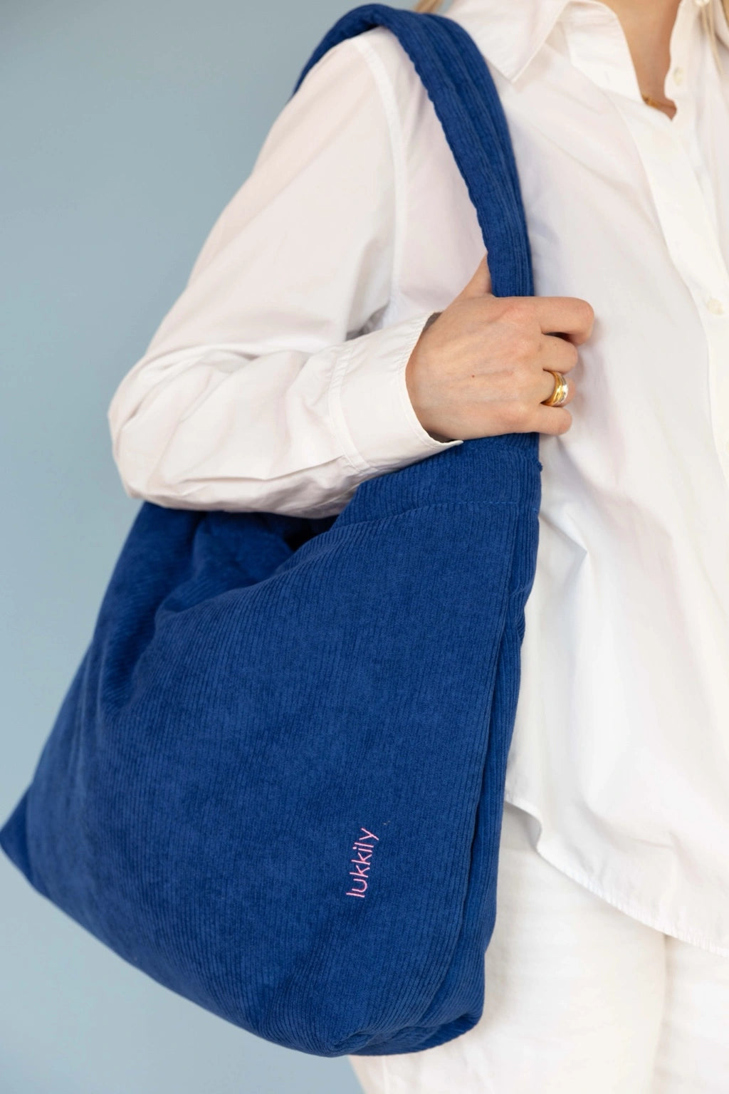 Lukkily Tote Bag Cord cobalt - hier am längenverstellbaren, gepolsterten Schultergurt als Schultertasche getragen, sodass die schöne pinke Logostickerei besonders gut zu sehen ist