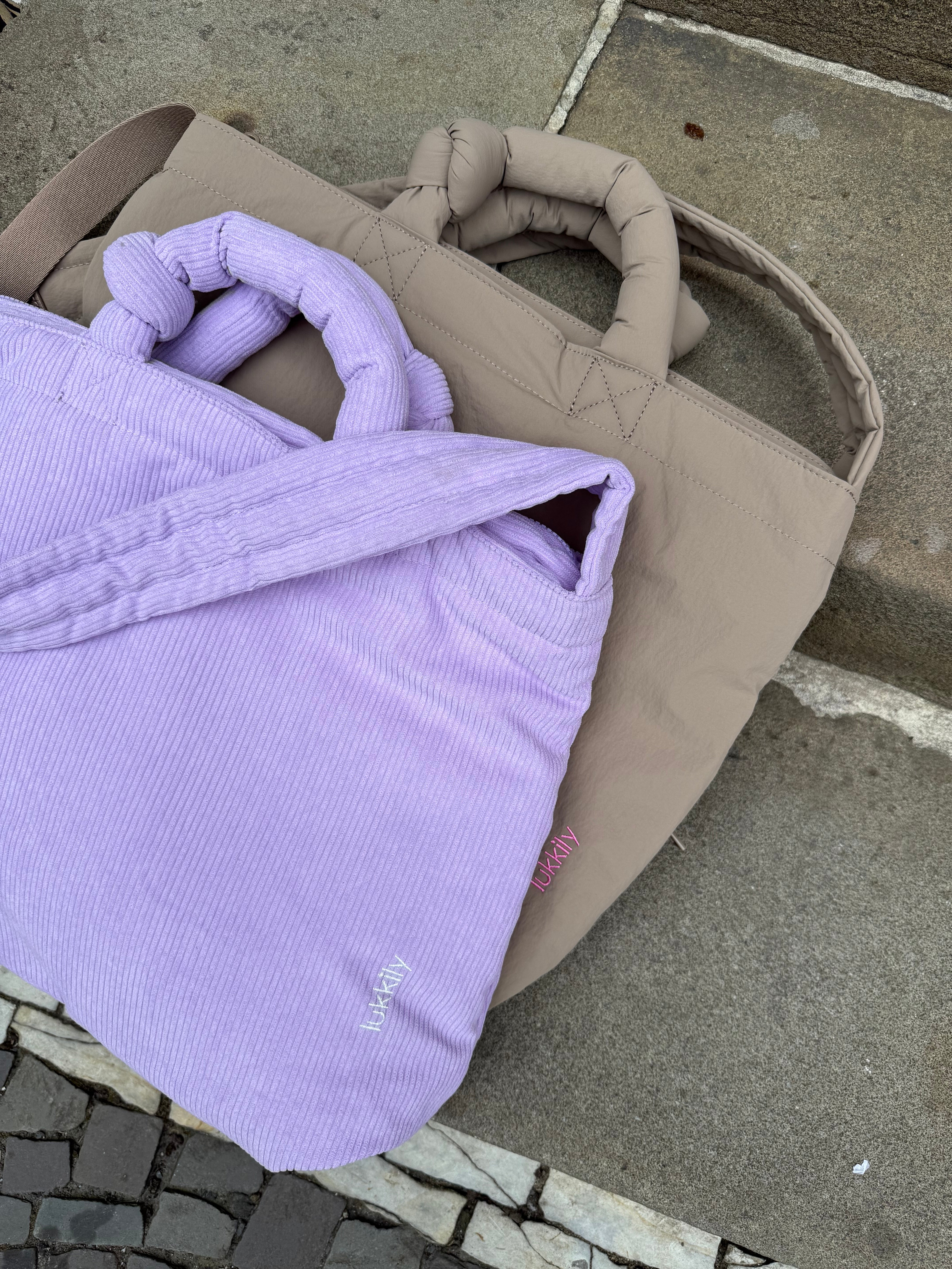 Vergleich zweier Lukkily Mom Bags: Cord Wickeltasche in Lilac und Nylon Umhängetasche in Taupe.
