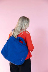 Lukkily Tote Bag Cord cobalt - Die blaue Cordtasche mit dem pinken lukkily Logo lässig auf den Rücken geschoben wie hier hat man die Hände frei für die Kids, den Einkauf oder das Lastenrad.