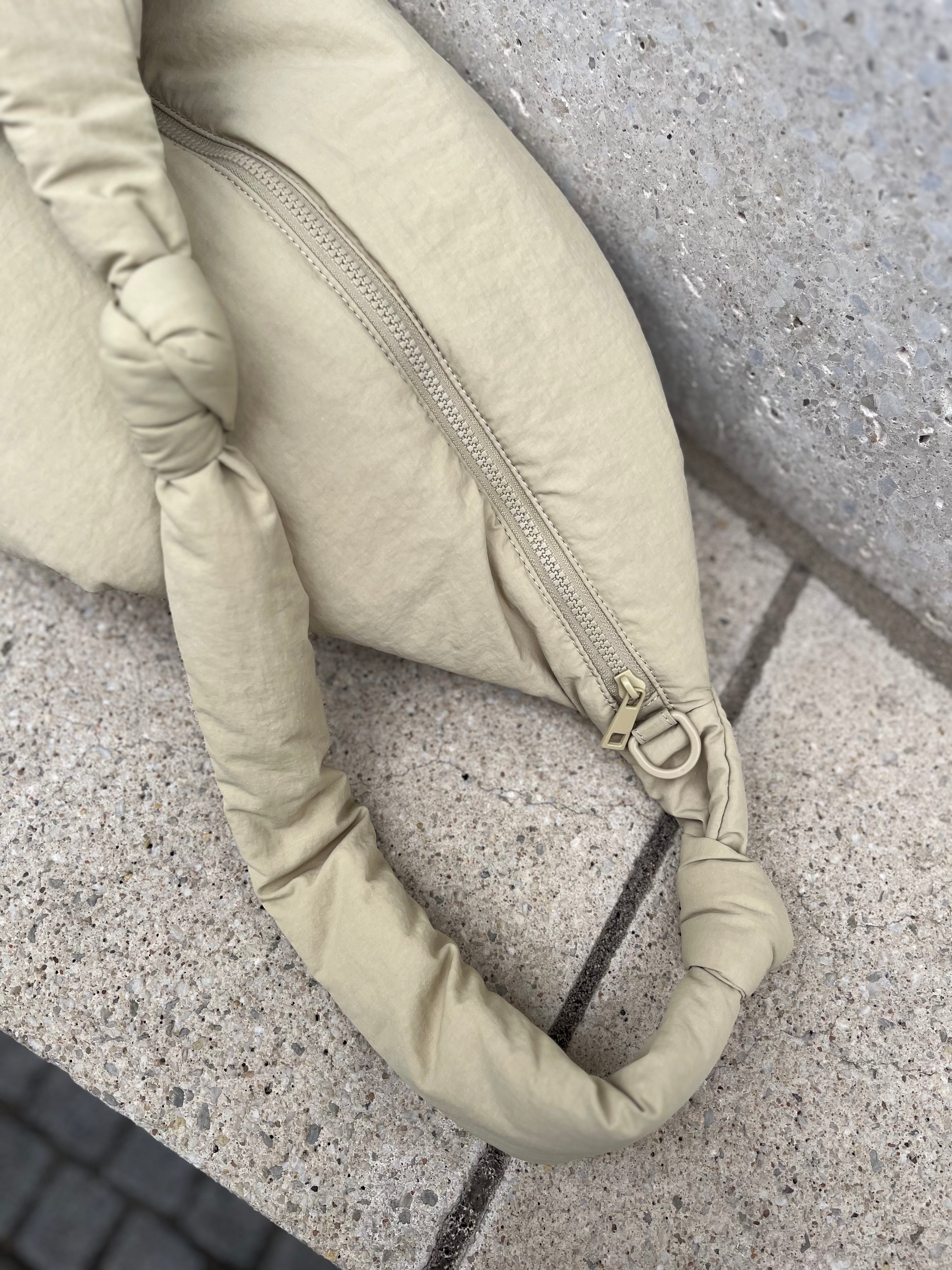 Nahaufnahme des Materials der Wickeltasche aus wasserabweisendem, beigen Nylon mit farblich passendem Reiverschluss und Öse zur Anbringung der Kinderwagenstraps