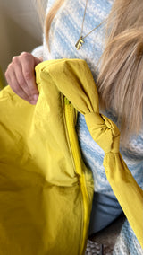 Close up vom matten, wasserabweisenden Material der Mombag in gelb mit farblich passendem Reißverschluss und Knotendetail als Designelement am Henkel