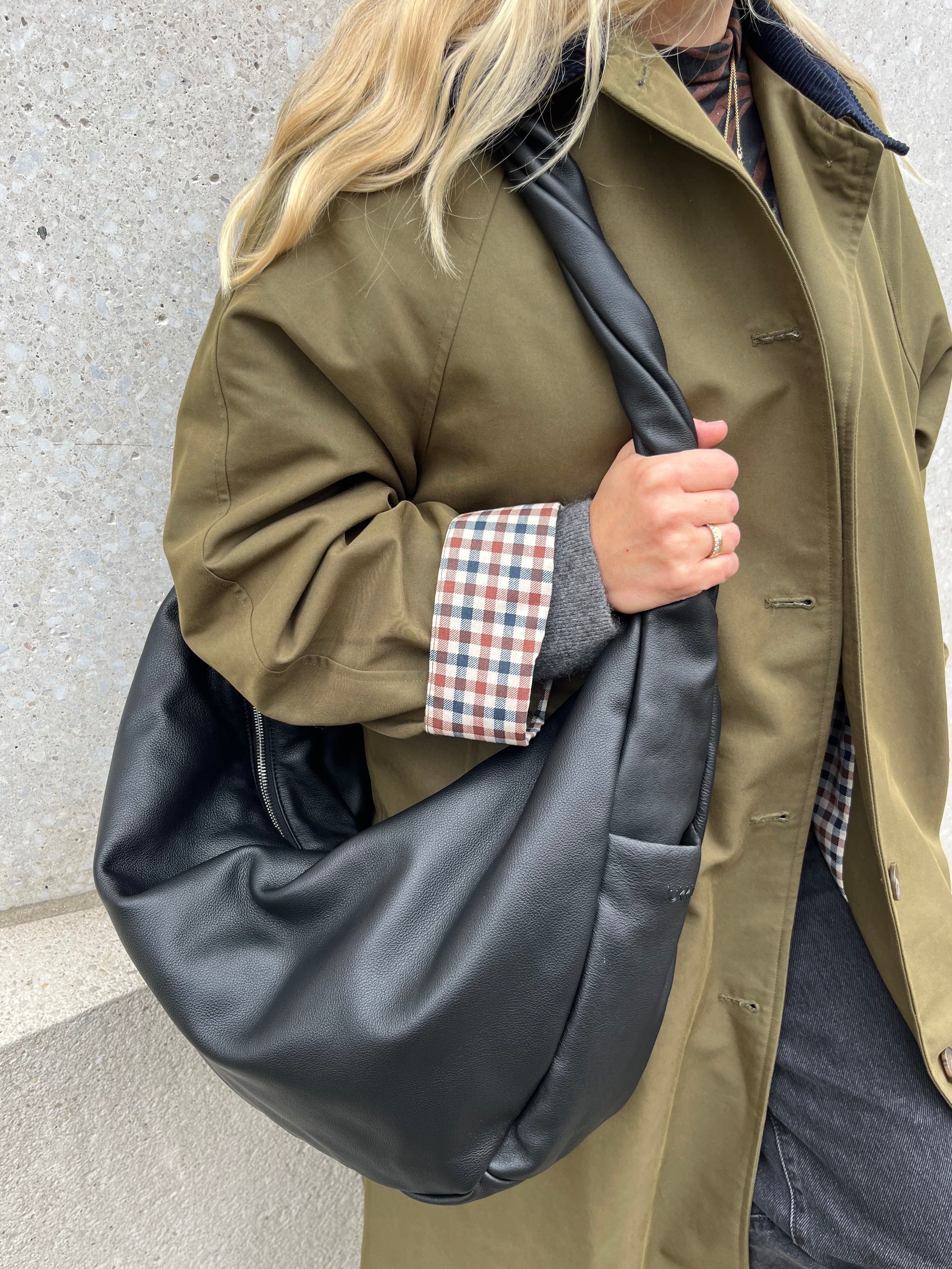 Softe Glattledertasche in schwarz als Schultertasche getragen mit silbernem Reißverschluss und in sich gedrehten Henkel als Designhighlight