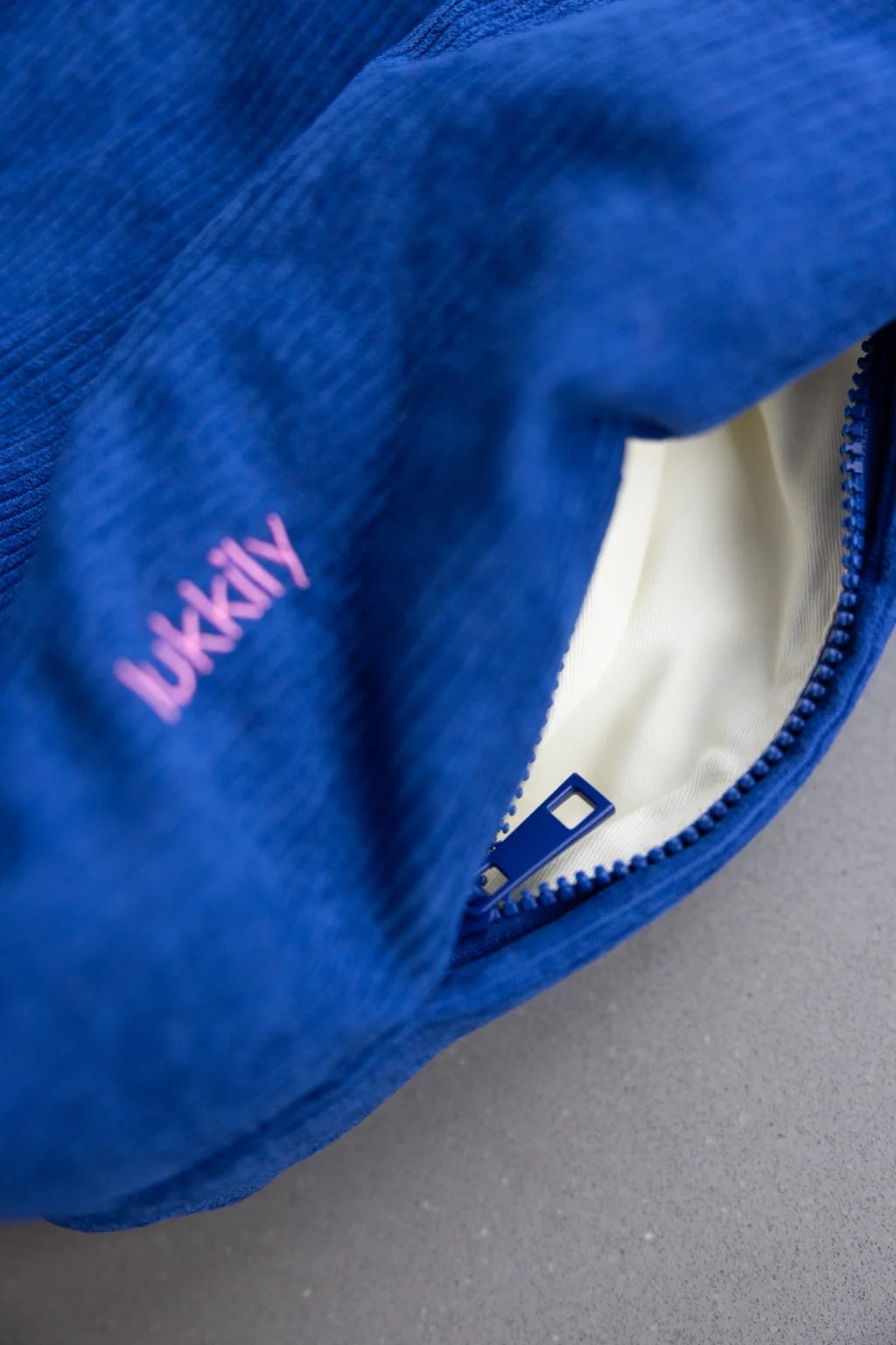 Lukkily Tote Bag - Detailaufnahme des blauen Cordstoffs mit pinker Logostickerei und Außenfach mit Zip