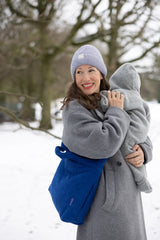 Mama mit blauer Lukkily Wickeltasche in Cordoptik crossbody getragen über einem Mantel mit Baby auf dem Arm