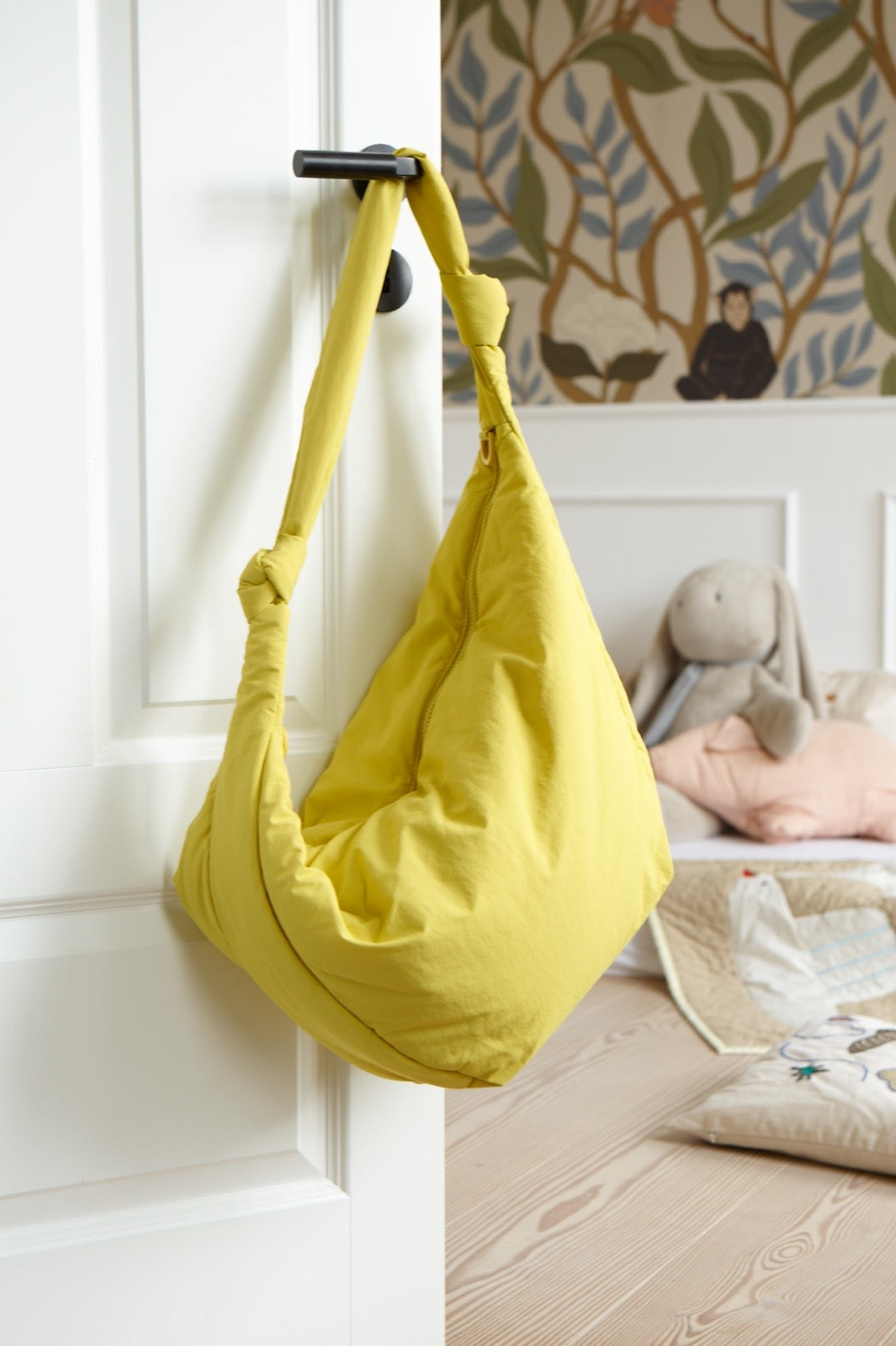 LUKKILY Bag #1 aus gelbem wasserabweisenden Nylon mit geknotetem Henkel, an der Türklinke eines liebevoll eingerichteten Kinderzimmers