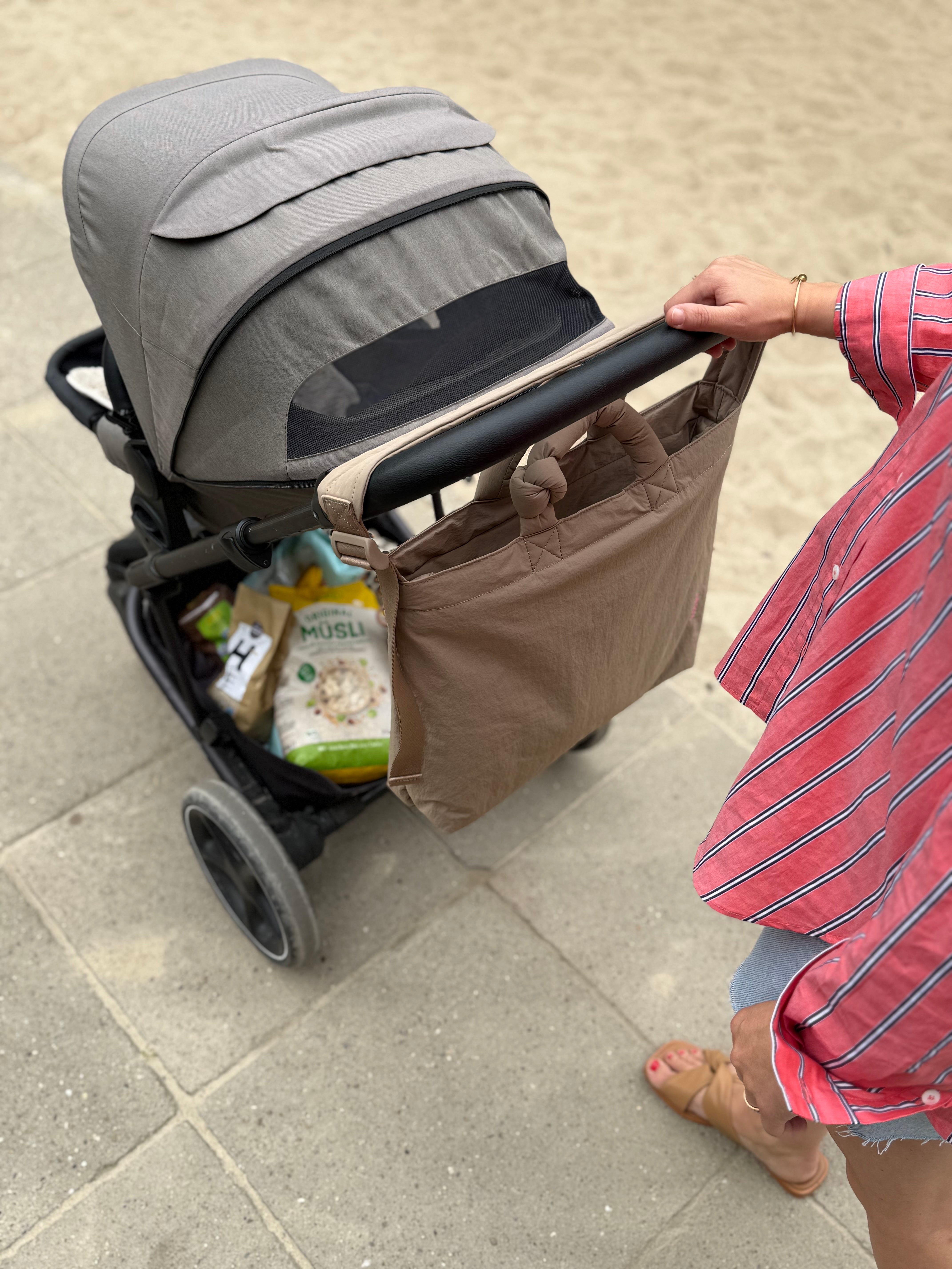Mama schiebt Kinderwagen mit cooler Wickeltasche in monochromen, beigen Look am Kinderwagenbügel