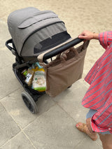 Mama schiebt Kinderwagen mit cooler Wickeltasche in monochromen, beigen Look am Kinderwagenbügel