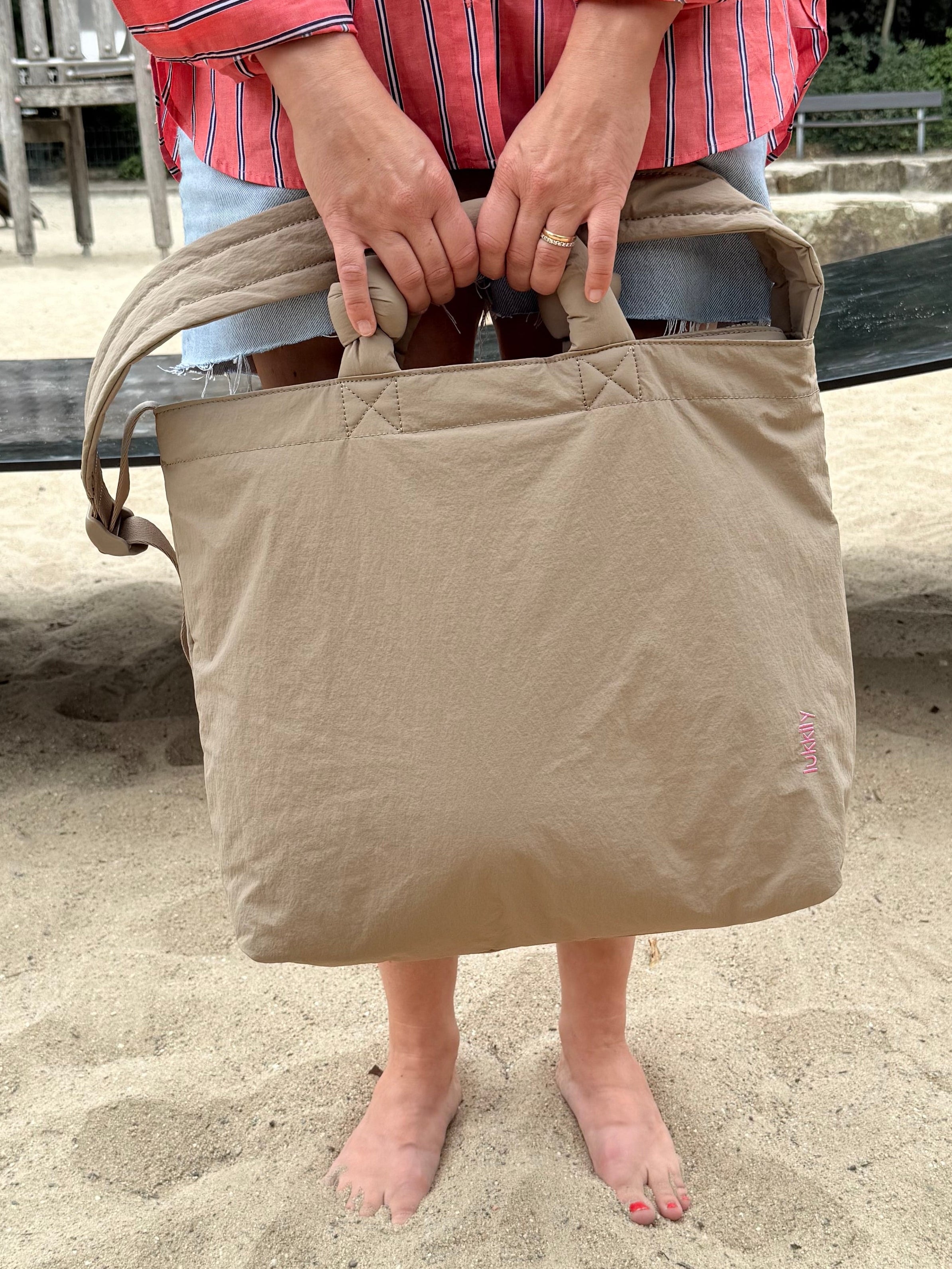 Sommerlicher Momlook mit cooler, beiger Mombag, die sich flexibel tragen lässt, auf dem Spielplatz