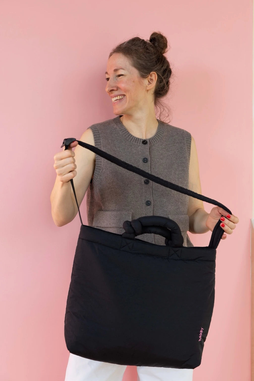 Lukkily Gründerin Laura hält sportive Crossbody Bag aus schwarzem Nylon mit Knotendetail am Henkel und langem Crossbody-Gurt zum Verstellen im cleanen minimalistischen Look