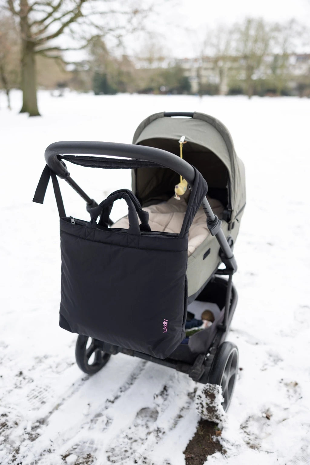 Stylische Kinderwagentasche im Tote Bag Format aus schwarzem Nylon mit längenverstellbarem Henkel und pinker lukkily Logostickerei 