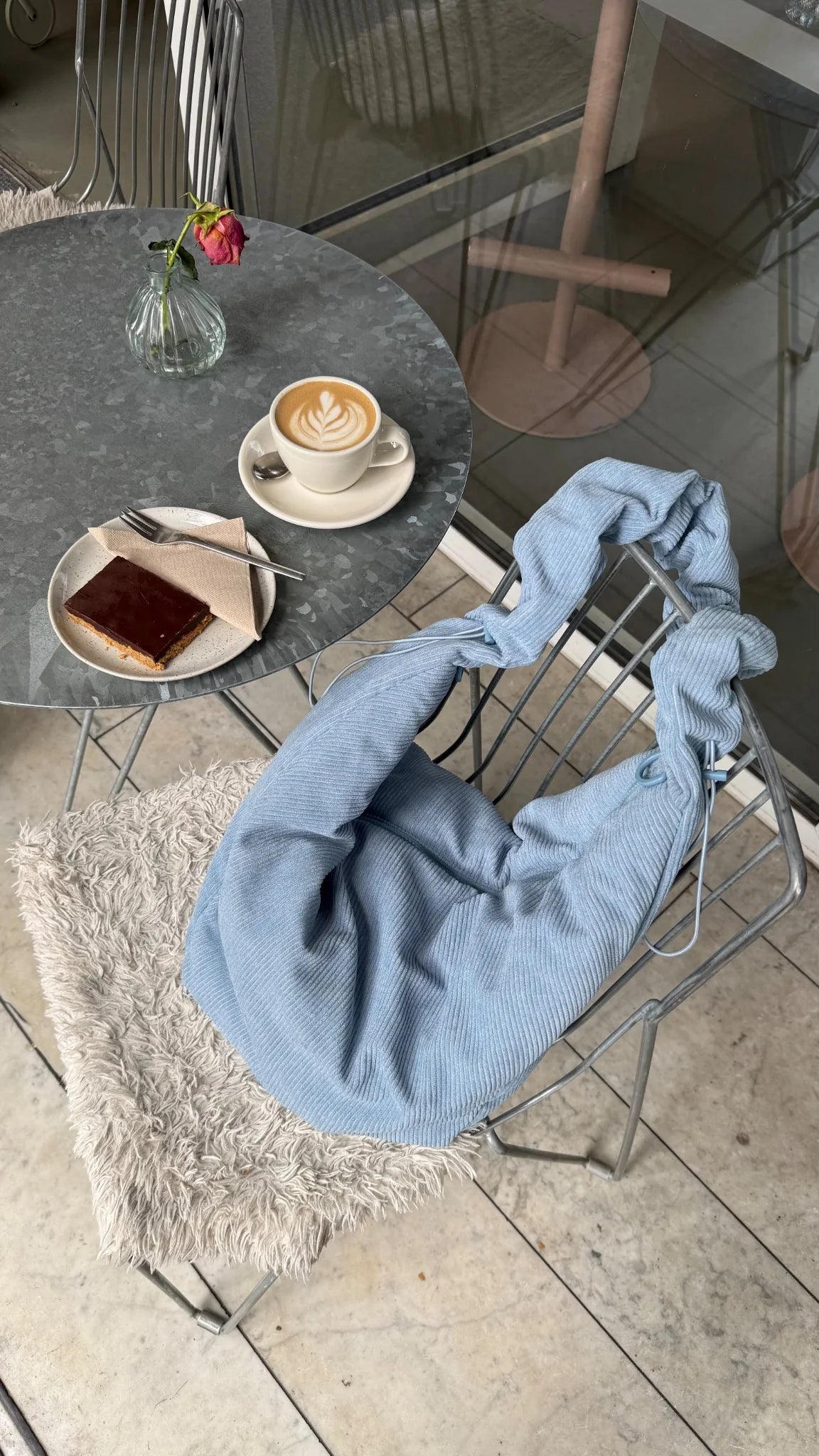 Lukkily Ruffle Bag aus weichem Cord in hellbau auf einem Stuhl in einem stylischen Café als Everydaybag