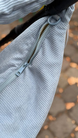 Close up vom Reißverschluss zum Verschließen der Wickeltasche, sowie des Rings zum Anbringen von Kinderwagenstraps - alles monochrom in hellblau.