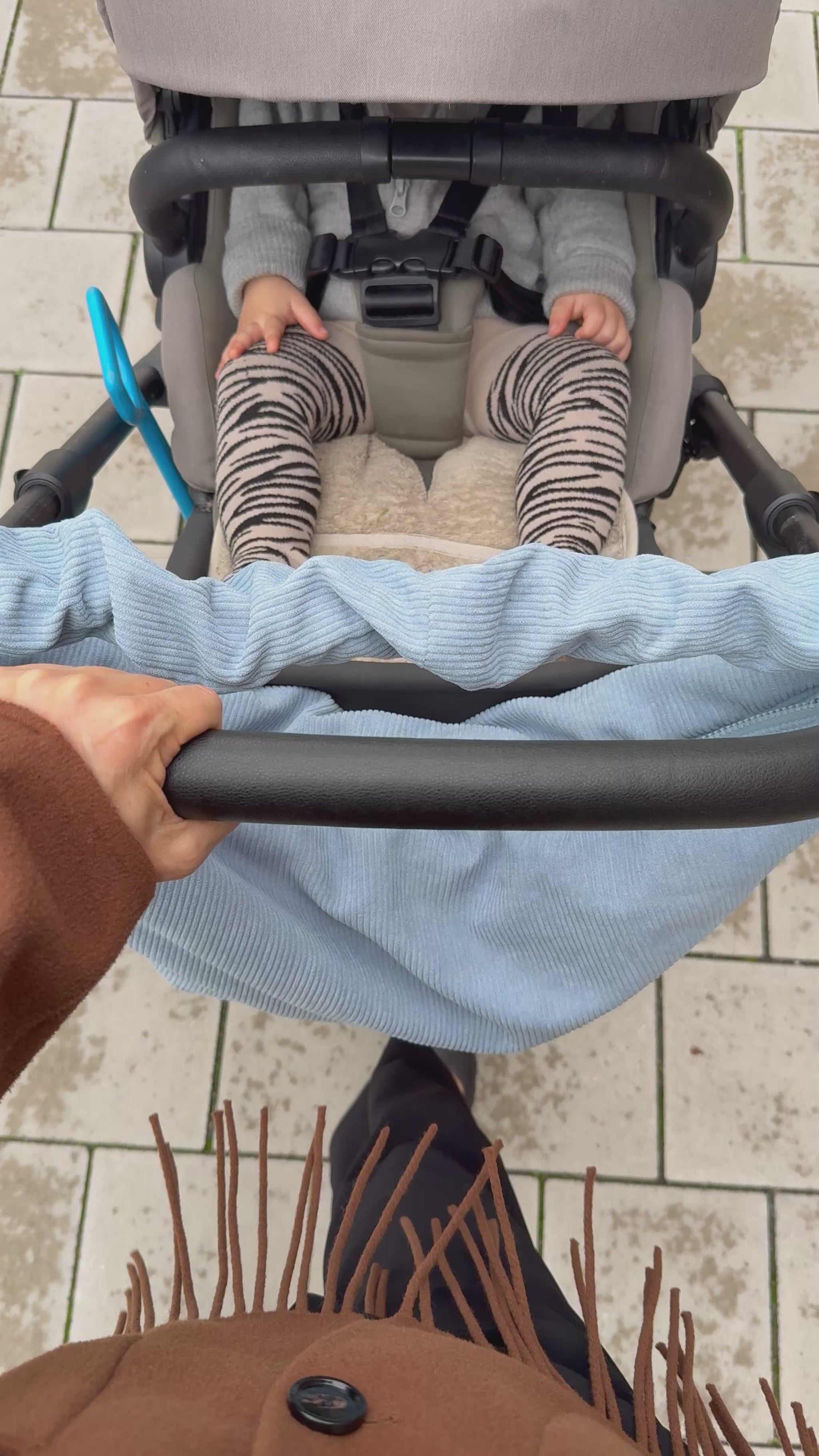 Mombag aus hellblauem Cord mit gerafftem Henkel am Kinderwagen, der von einer stylichen Mama geschoben wird